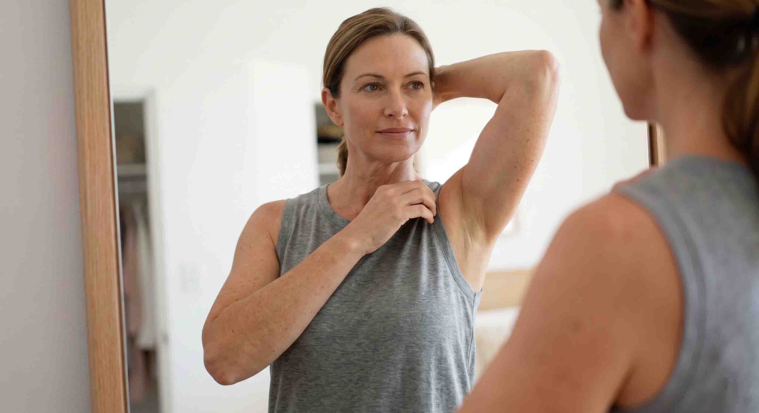 Mujer de mediana edad observando resultado braquioplastia en espejo.